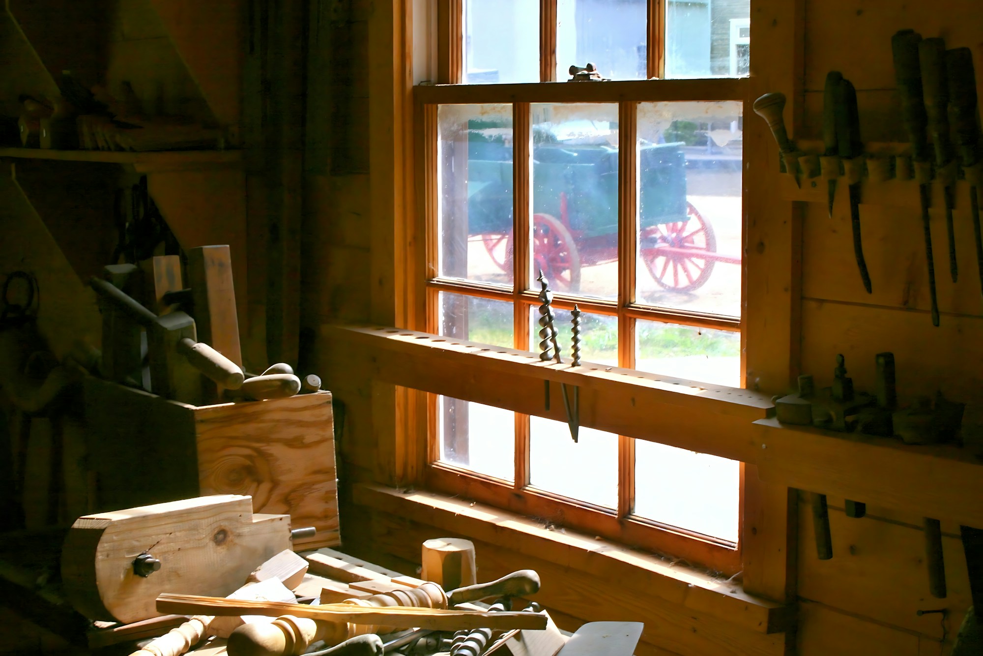 Woodworking bench with hand tools and offcuts in front of a sunlit workshop window