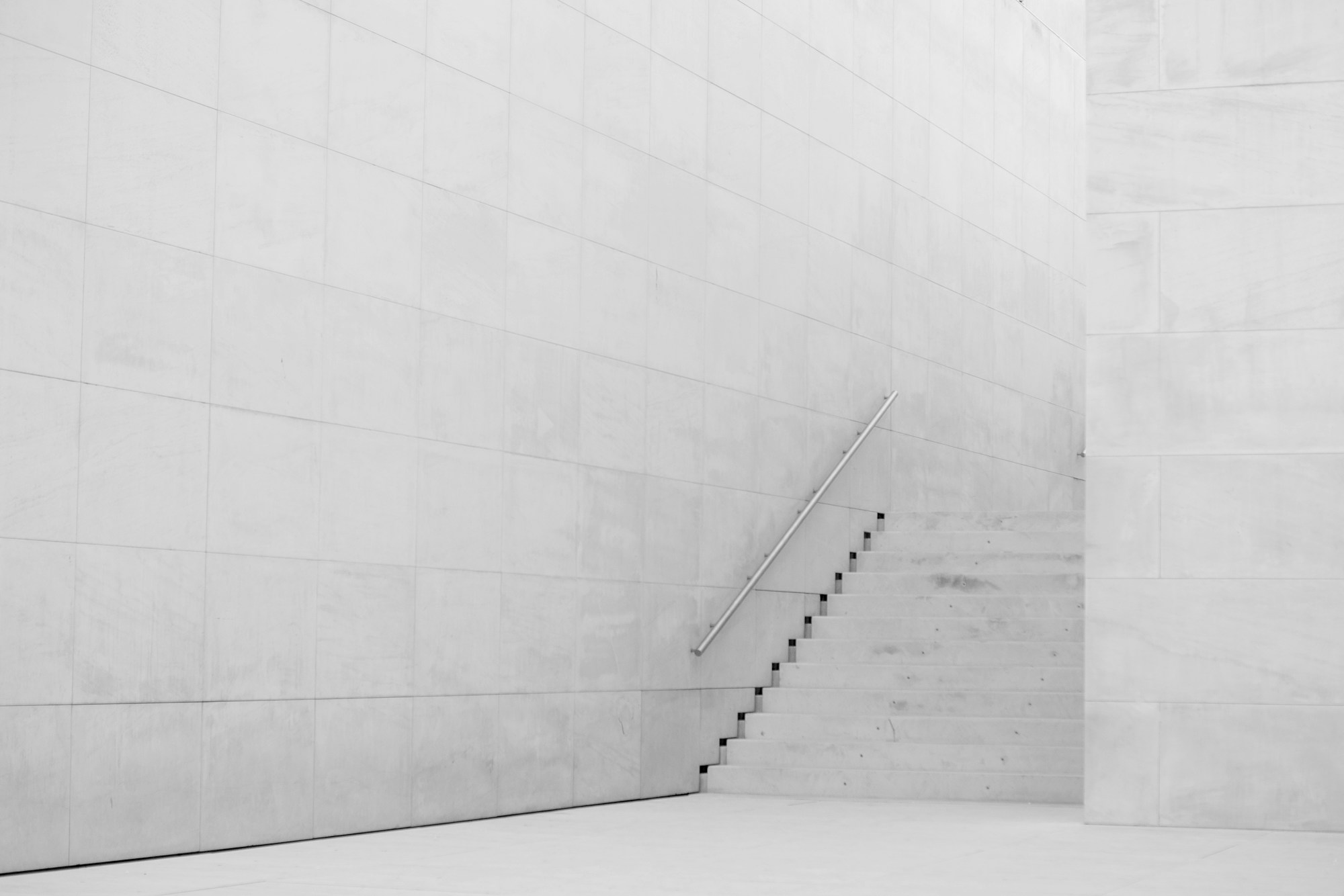 Escalier en béton épuré longeant un mur clair, avec une rampe métallique fine en diagonale
