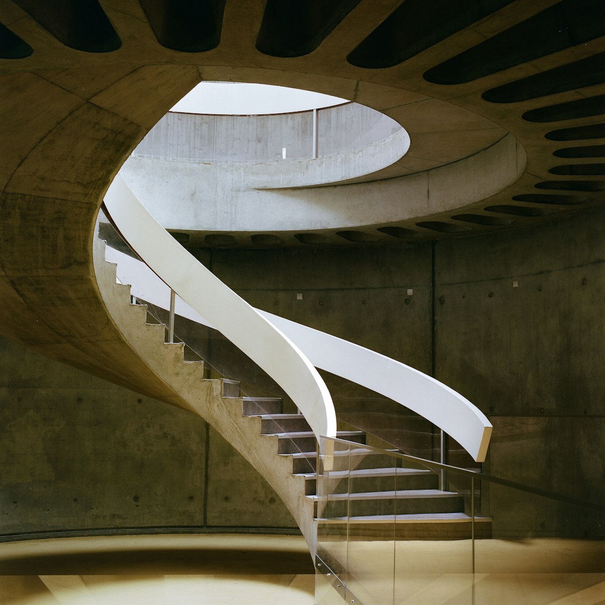 Escalier en béton en spirale avec garde-corps blanc s’élevant vers un puits de lumière rond