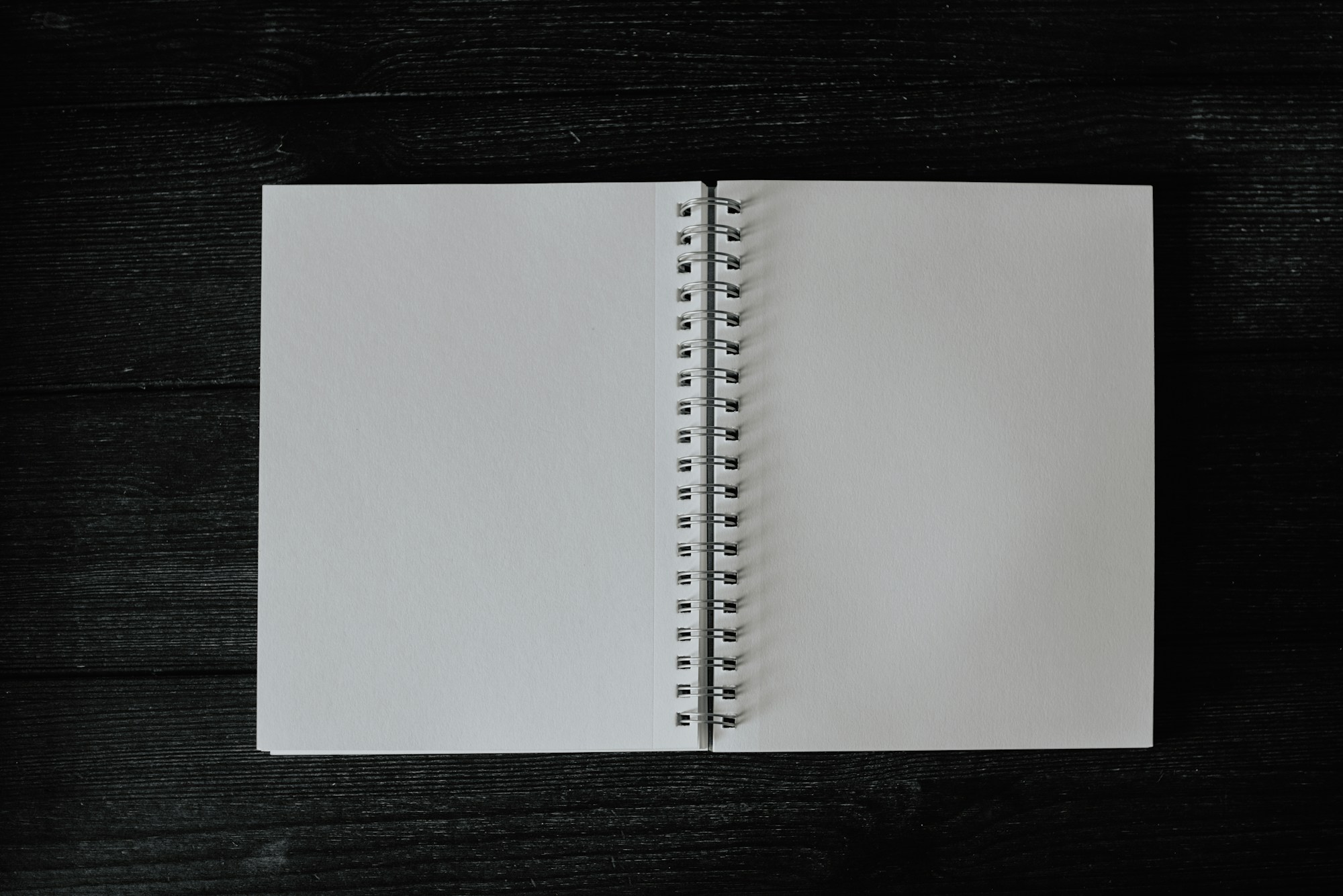 Aufgeschlagenes Spiralnotizbuch mit leeren Seiten auf einem dunklen Holztisch