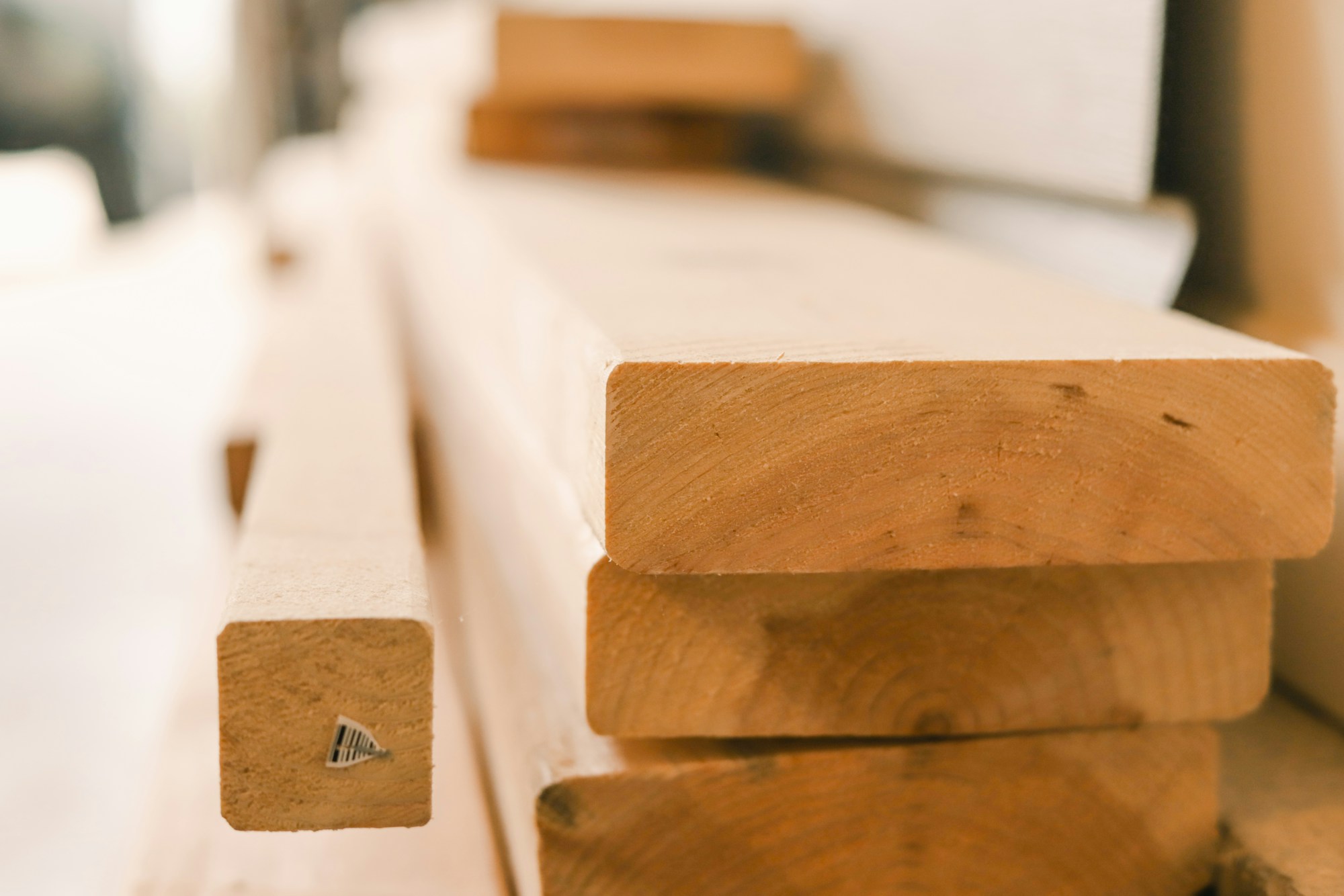 Planches de bois rabotées empilées en gros plan dans un atelier, un tasseau plus fin posé devant, arrière-plan flou