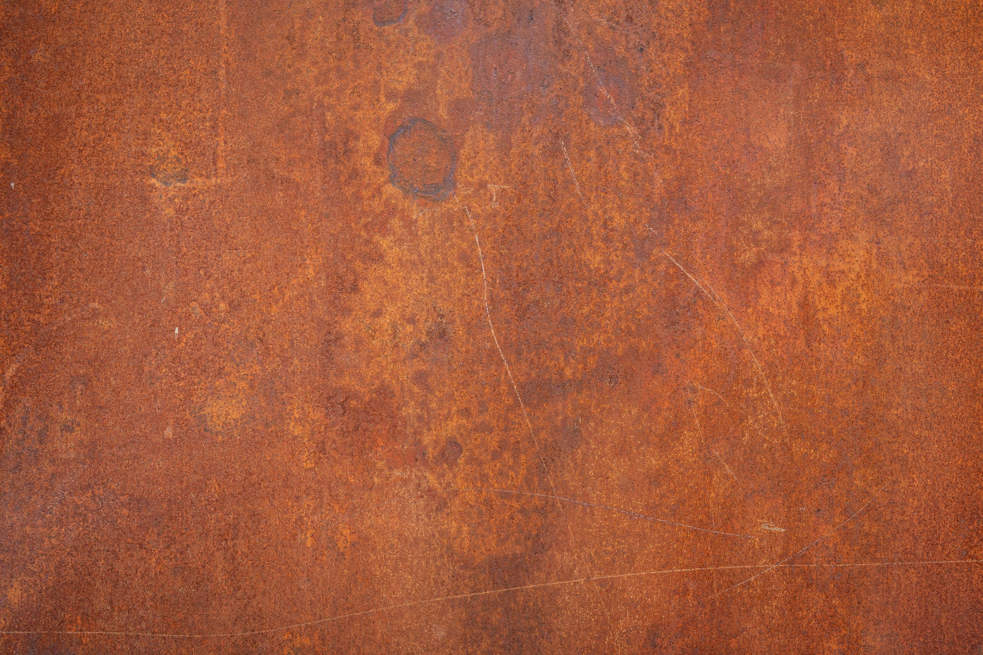 Close-up of a weathered metal sheet in copper and rust tones, with faint scratches across the surface