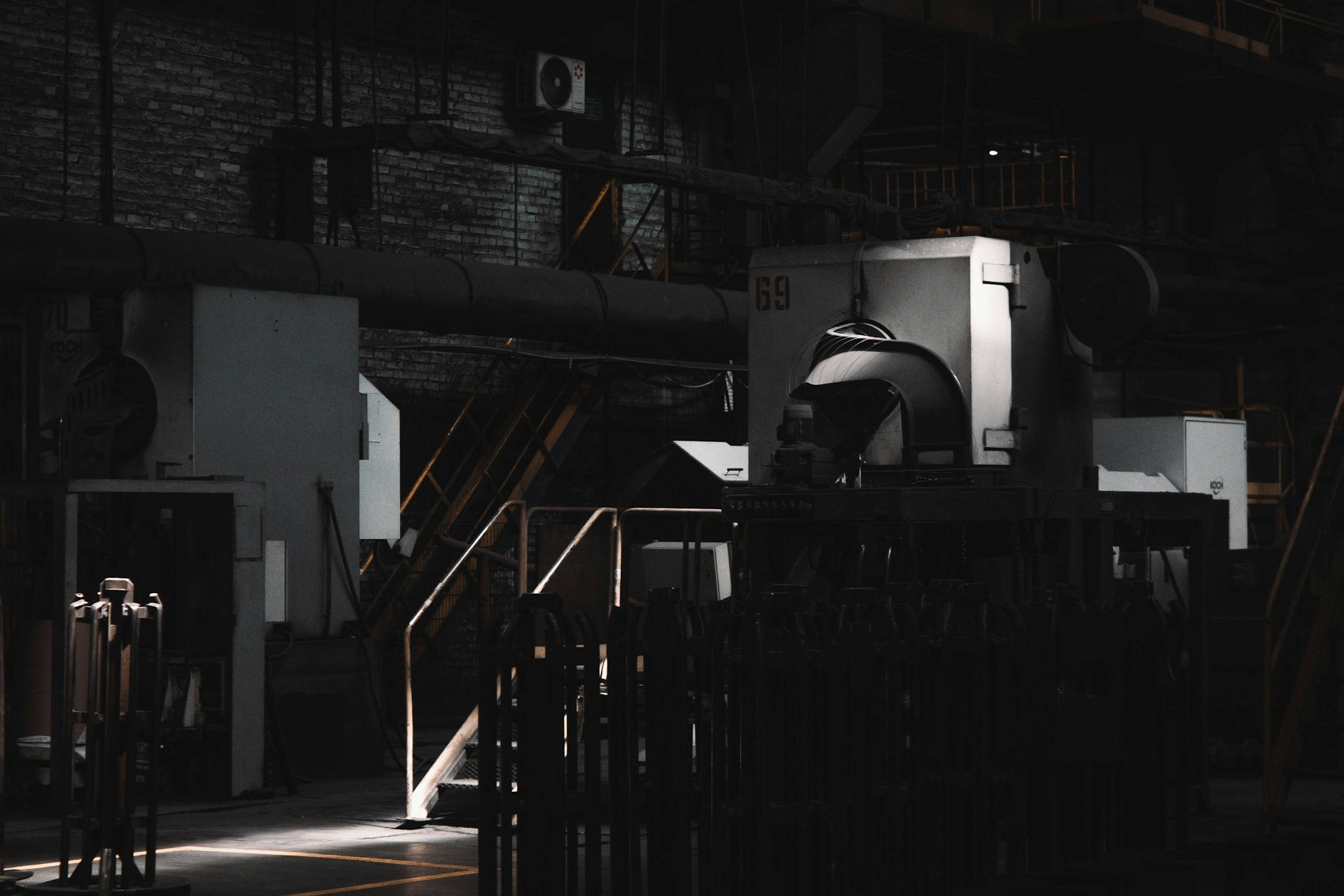 Atelier industriel plongé dans la pénombre, machines et gaines métalliques éclairées par une lumière rasante
