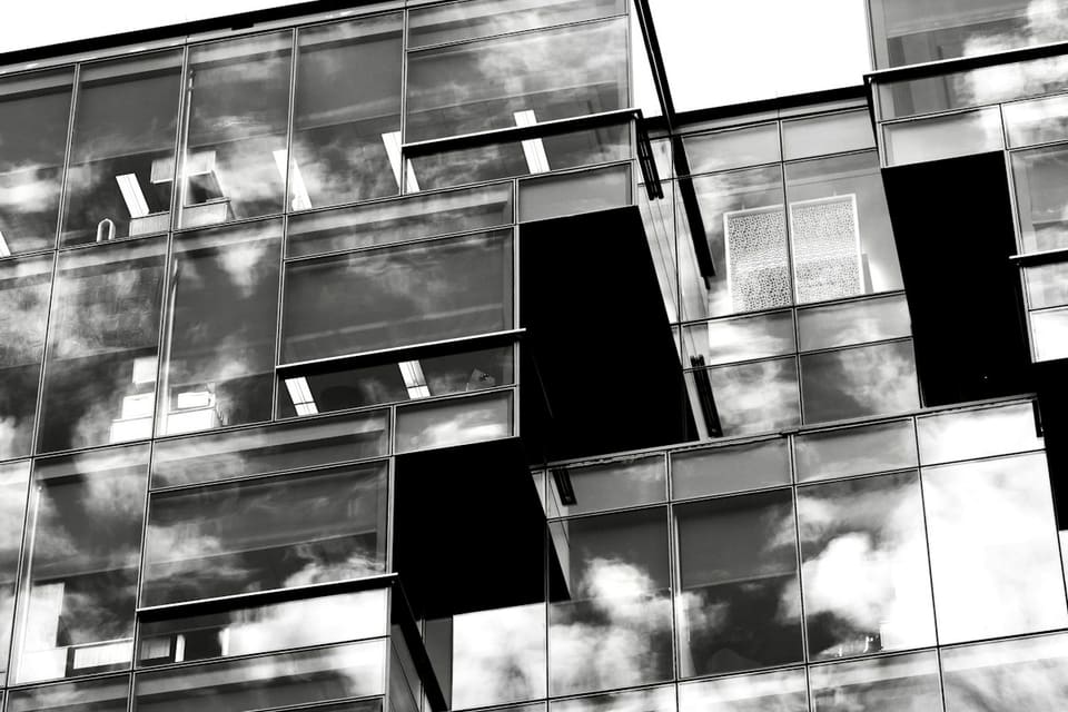 Glasfassade eines Bürogebäudes in Schwarzweiss, versetzte Baukörper spiegeln Wolken