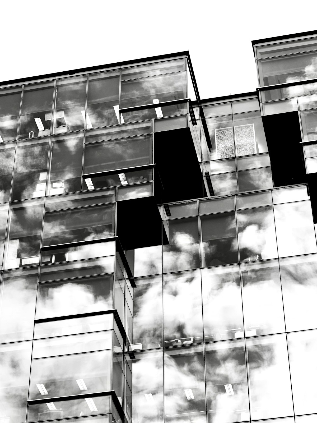 Black and white glass office facade with offset, jagged volumes reflecting clouds