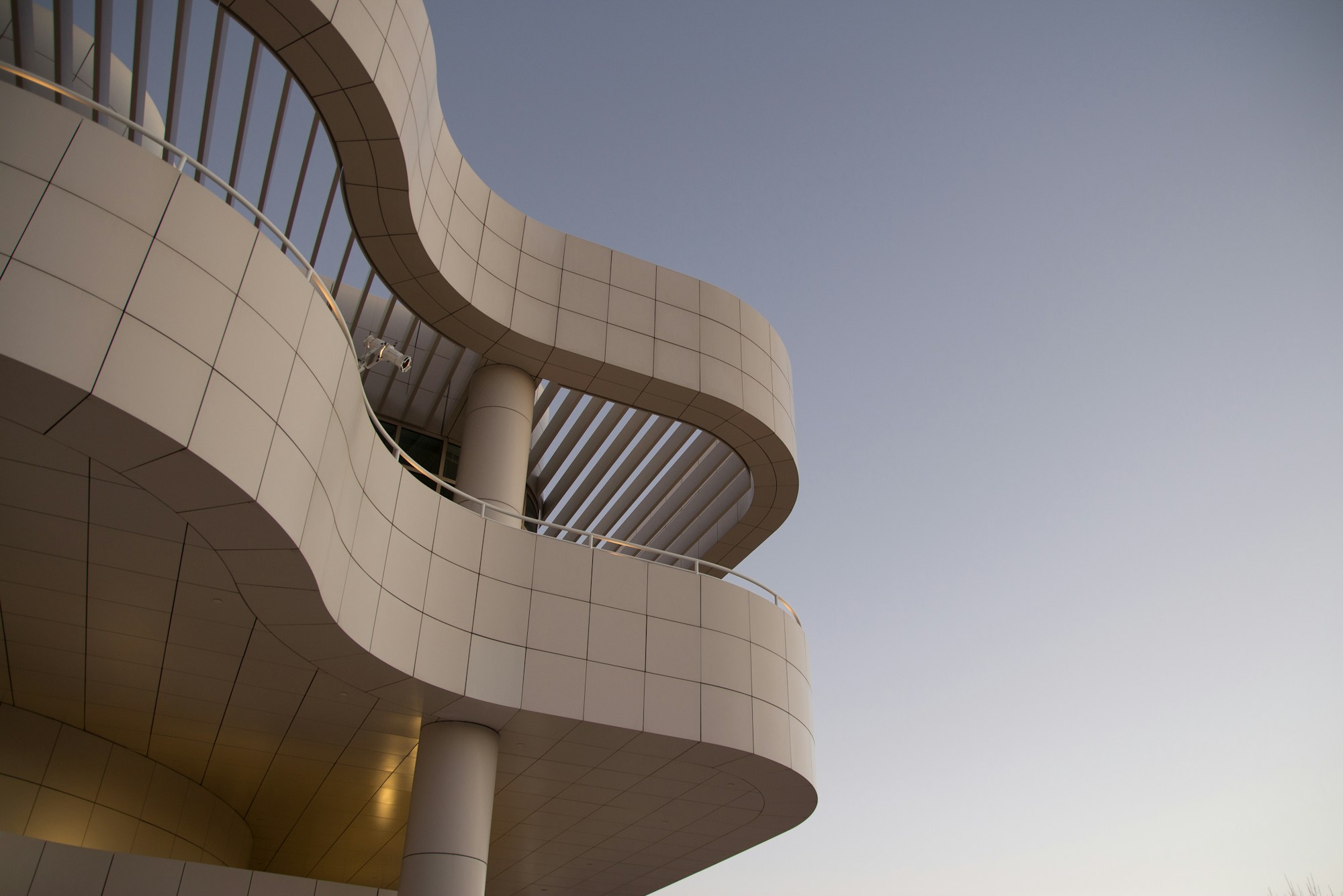 Curved terraces of a modern building with pale panels, seen from below in soft evening light