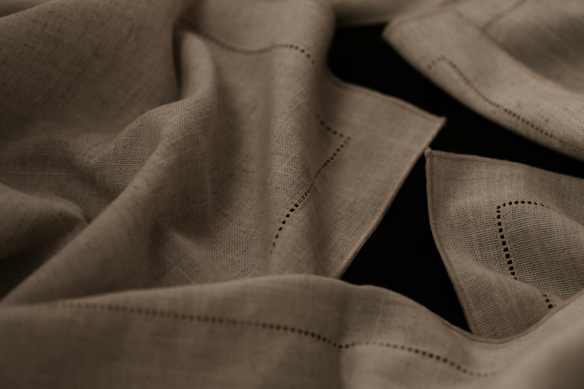 Close-up of folded natural linen napkins with hemstitched borders on a dark surface