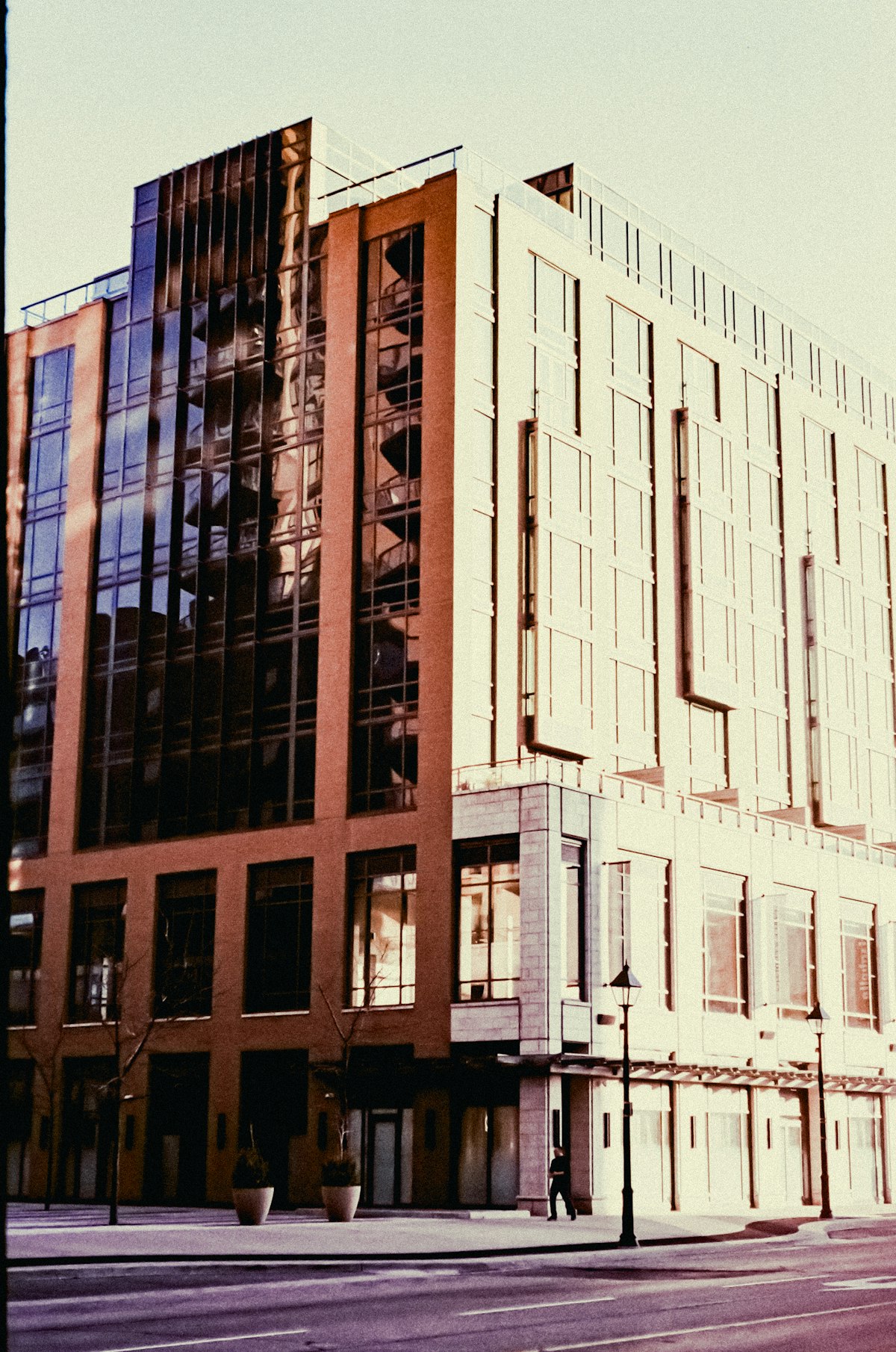 Angle d’un immeuble de bureaux moderne, façade vitrée dans une lumière chaude au-dessus d’une rue calme