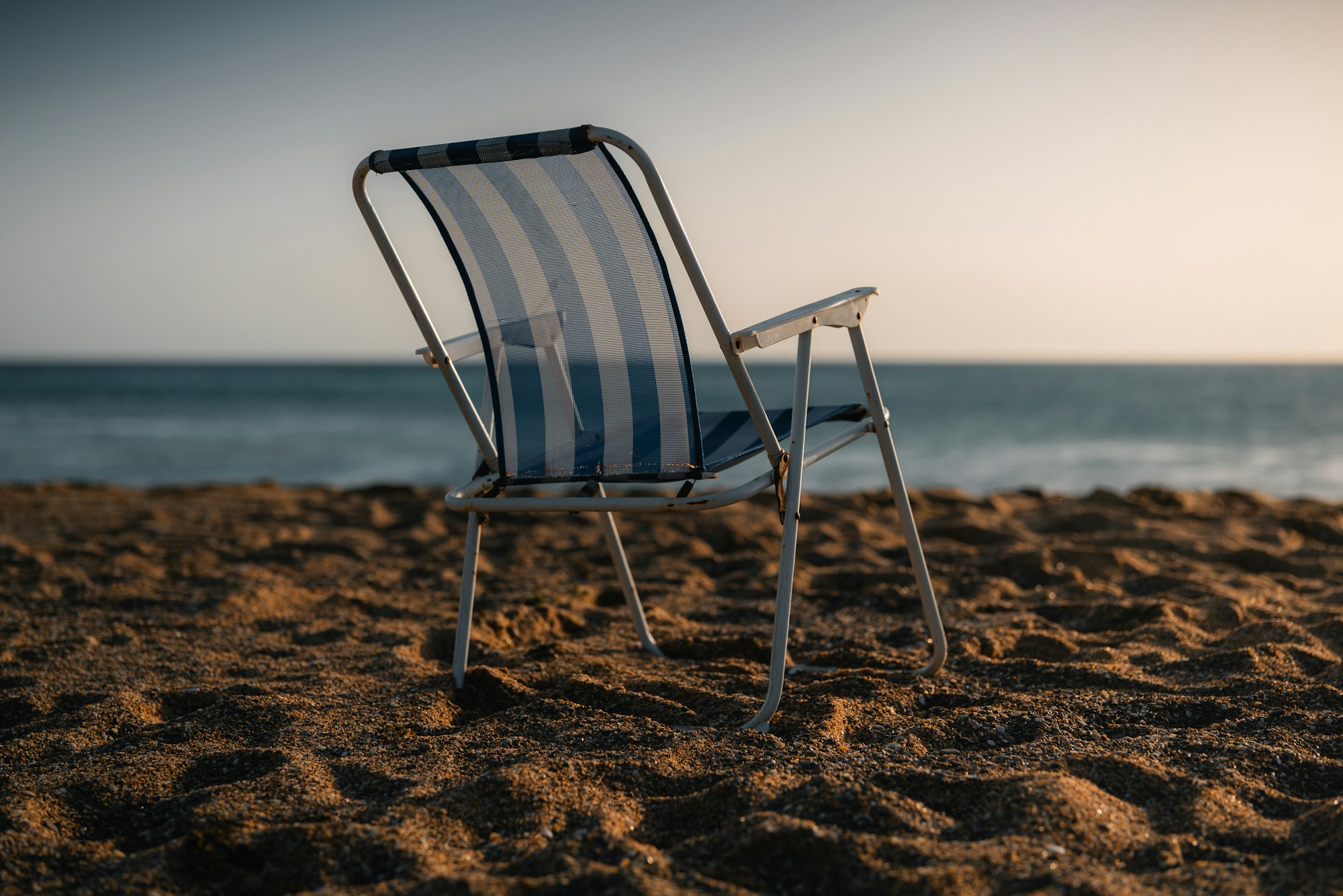 Chaise de plage pliante rayée, vide, face à la mer à la lumière du soir
