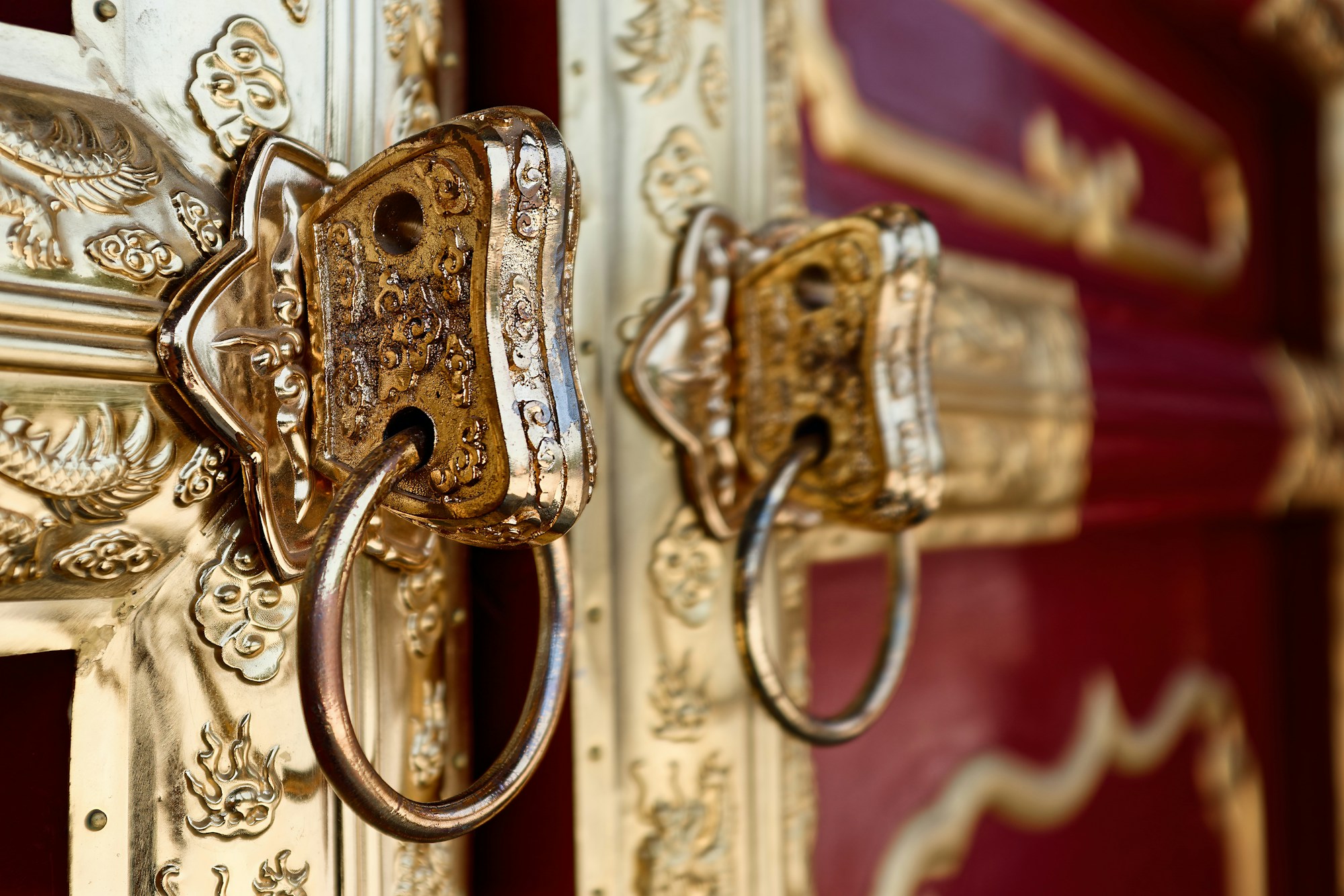 Close-up of two gilded ring handles on ornate brass-plated red lacquered doors