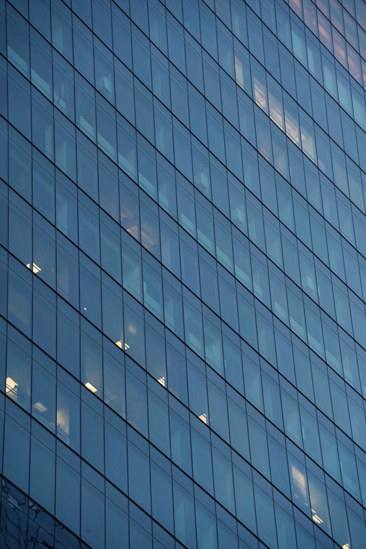 Blau getönte Glasfassade eines Bürohochhauses in der Dämmerung, einzelne Fenster erleuchtet