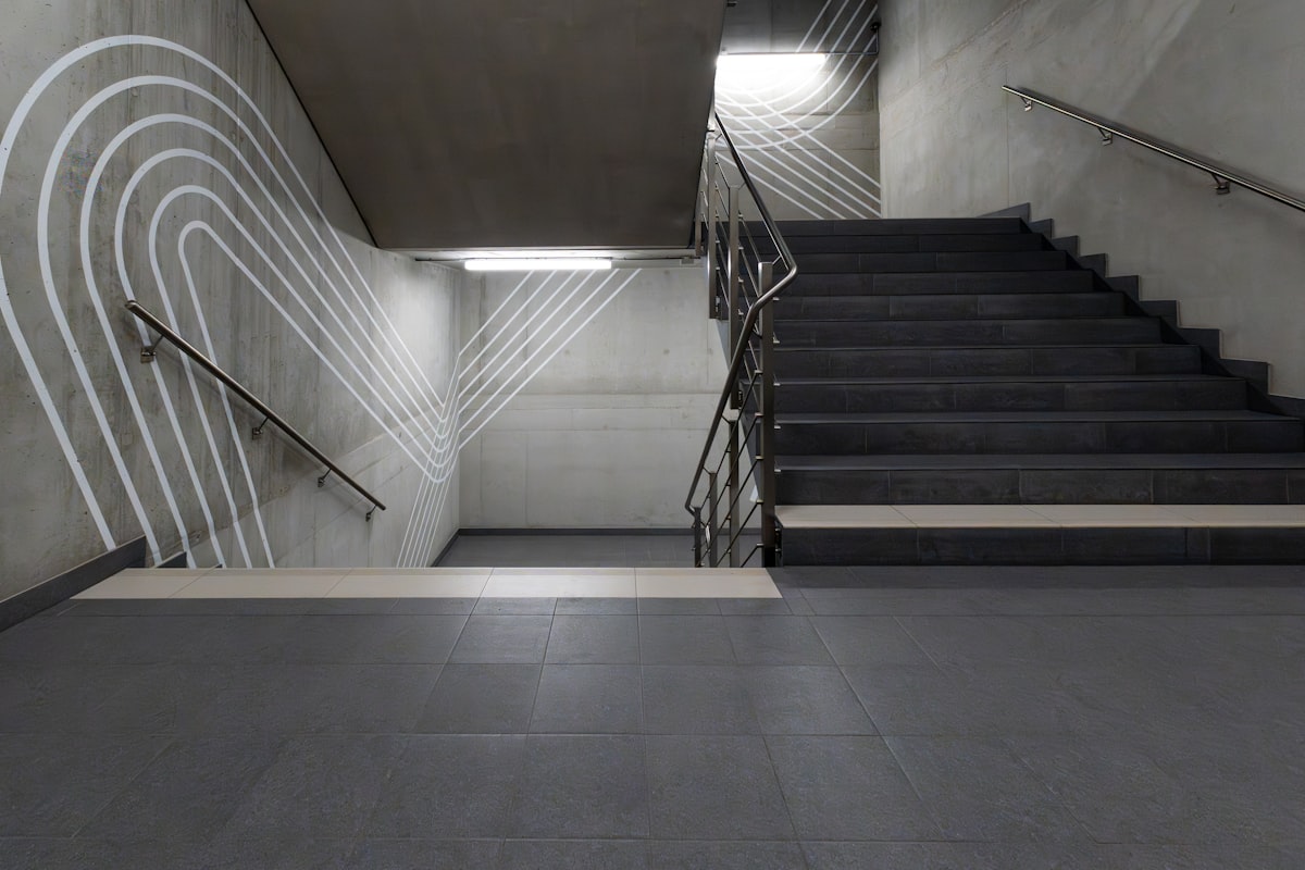 Betontreppenhaus mit einer Treppe nach oben und einer nach unten, weisse geschwungene Linien an der Wand