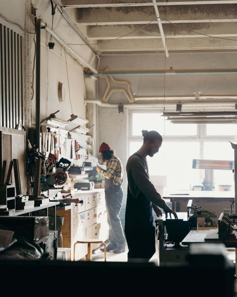 Two people at work in a bright workshop, each at their own bench